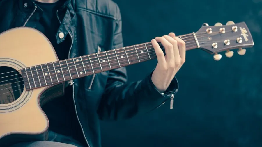 Young person learning to play acoustic guitar indoors with natural lighting